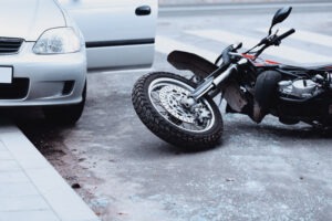 a-motorcycle-lying-in-the-road-beside-a-car-with-its-door-open-after-an-accident