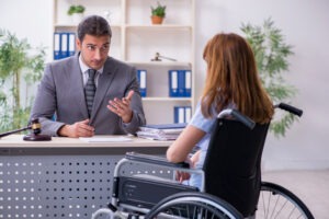 Lawyer sitting at desk explains personal injury claim process to woman in wheelchair.