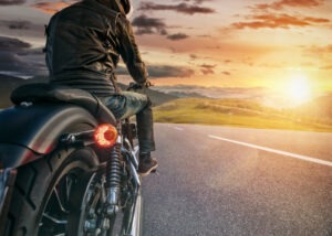 A motorcyclist rides their motorcycle down the road into a mountainous sunset.