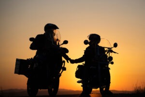 Two motorcyclists hold hands against a sunset.