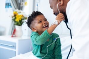 A laughing little boy in a hospital bed interacts with his father.