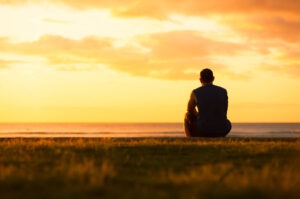 A young man sits and grieves against a sunset.