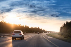 A lone car drives down a highway at sunset.