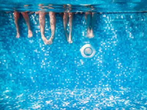 Faceless adults and children stick their legs in a swimming pool.