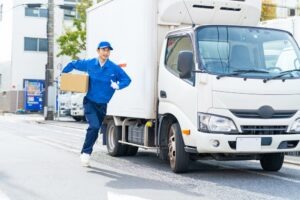 A postman rushes away from a delivery truck to place an unlabeled brown box on someone’s doorstep.