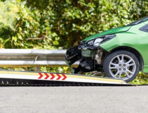 A green car sits on the side of the interstate after a collision that damaged its hood.