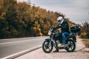 A helmeted motorcyclist pulls over to the side of the road on an empty highway.