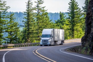 A truck driver navigates a white cab and trailer around a tight corner on the interstate.