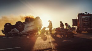 Firefighters put out a fire at the scene of a car accident as the sun sets.