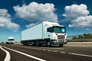 Two white trucks drive down an empty highway.