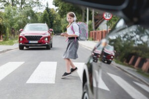 A rideshare drives toward a young child at an intersection.