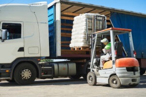 A forklift driver carefully loads a semi truck.