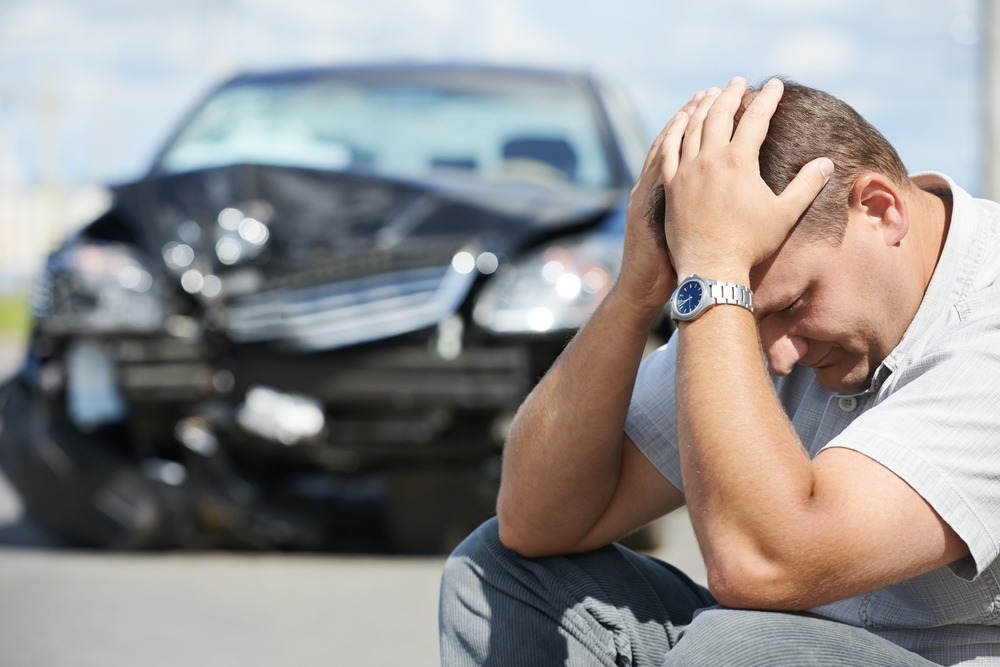 Man with his head in his hands sitting in front of his damaged car after an auto accident on one of the top five most dangerous highways in the Midwest