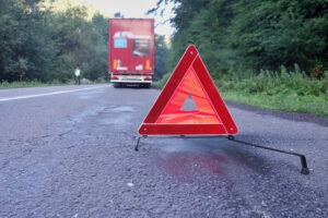 A red warning triangle on the road behind a large truck. A lawyer can explain what the proper emergency triangle placement is for semi-trucks.