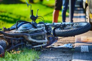 Severely damaged motorcycle lying on the road after a collision in Indianapolis with a bystander and car visible in the background representing need for a motorcycle accident lawyer in Indianapolis