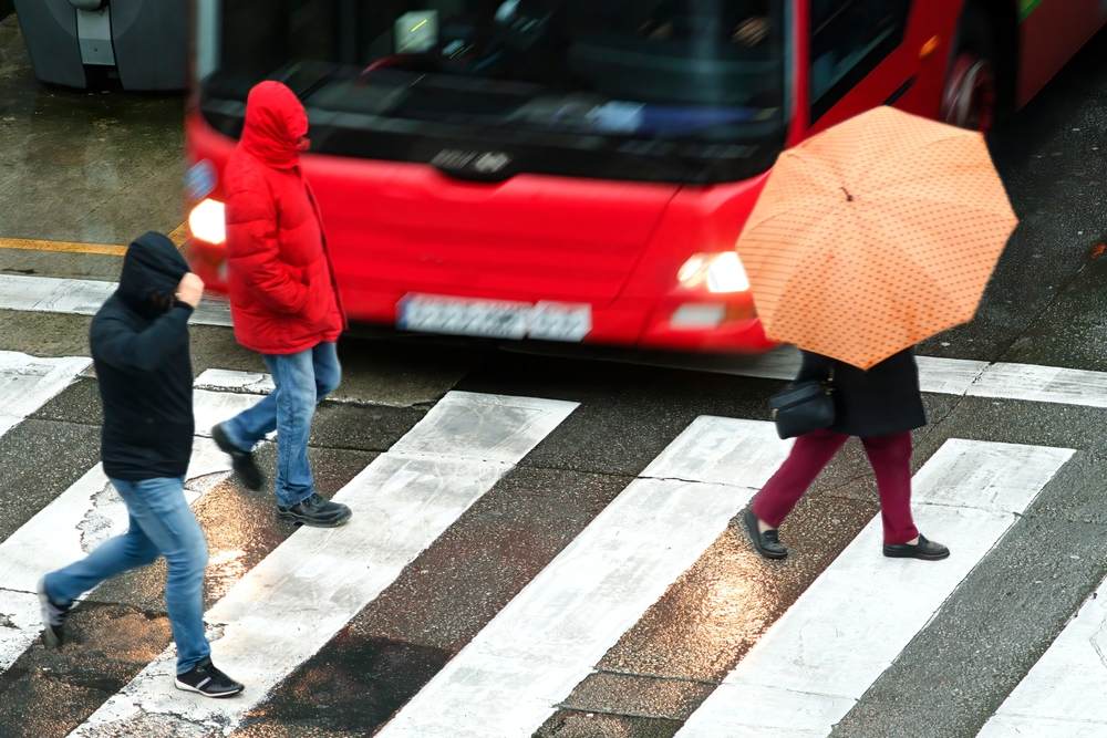 Pedestrians crossing a busy street in front of an oncoming bus during rainy conditions avoiding a pedestrian accident in Indianapolis